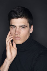one young handsome man, model wearing turtleneck, simple studio upper body shot, black background.