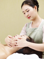 young asian masseur performing face massage on woman