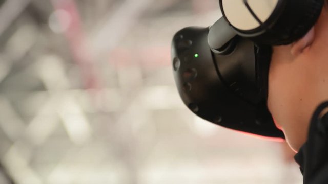 The guy plays in the VR headset virtual reality at a meeting events of computer game fans. In the background there are a lot of people in the blur, bright and lights from concert.