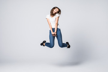 Smiling woman jumping in studio and looking at camera over gray background