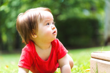 Happy baby boy in a red shirt crawling around outside