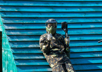 Boy in camouflage suit stands on the paintball field with his paintball gun up and looks straight ahead. team work, sport lifestyle