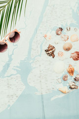 top view of seashells with sunglasses and palm leaves on travel map