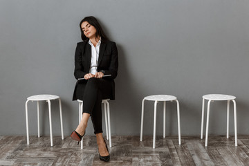 tired businesswoman in suit with laptop sleeping on chair while waiting for job interview