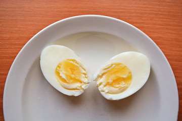 two halves hard boiled chicken egg and part white plate and wooden table 