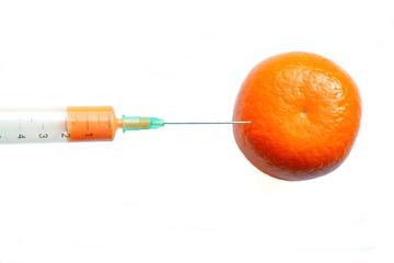 Injection of medical syringe with yellow liquid stuck in a fresh orange mandarin for growth....