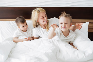 Obraz na płótnie Canvas Mom and her sons playing in the morning in bed.