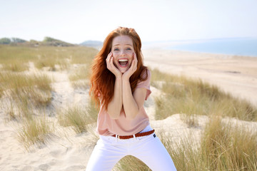 Hübsche rothaarige Frau in einer Dünenlandschaft begeistert Meer im Hintergrund