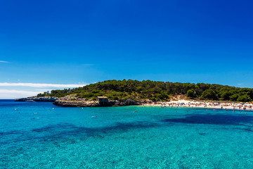 Beautiful beach with turquoise water crowded with tourists in Cala Mondrago, Mallorca