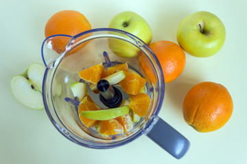 Pieces of juicy fruit in a blender. In the background, whole oranges and green apples. Concept- healthy food, vegetarianism. © 008melisa