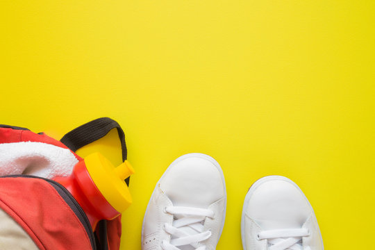 Woman's running accessories. White sneakers, red bag with towel and bottle of drink on yellow background. Empty place for text of sports motivation or workout program.