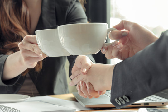 women cheers cups of coffe and chake hands after finish agreement