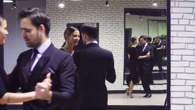 Portrait of professional dancing couple in black suits dancing tango in the ballroom. Two mirrors opposite each other create a lot of reflections