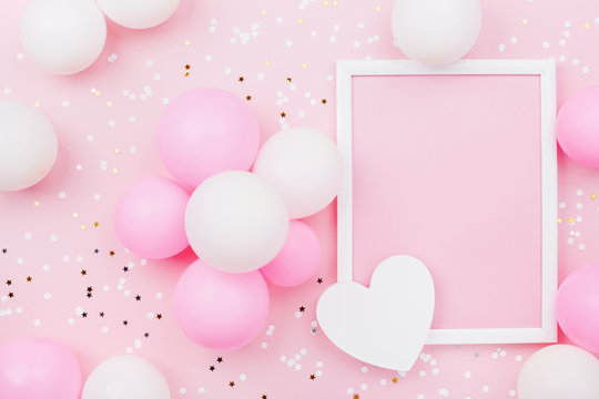Holiday or birthday mockup with frame, pastel balloons, heart and confetti on pink table top view. Flat lay composition.