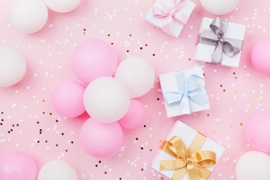 Birthday background with gift or present box, balloons and confetti on pink pastel table top view. Flat lay composition.