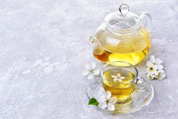 Glass teapot and teacup with green tea and spring flowers