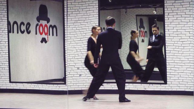 Professional dancing couple in black suits dancing tango in the ballroom. Reflection in the mirror.