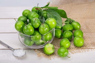 Close Up Of Green Plums Or Greengage in a glass bowl and sprinkle of salt Isolated On White wooden Background, Popular Spring Fruits With A Very Sharp Sour Taste Originated In Iran