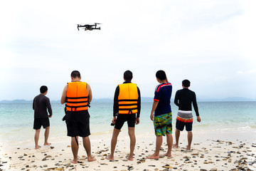 Group of friends standing on the beach and recording video with drone