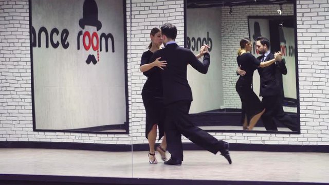 Professional dancing couple in black suits dancing tango in the ballroom. Reflection in the mirror.