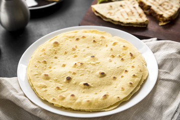 Mexican corn tortillas on a white plate on the dining table. In the background, hot quesadilla, closeup.