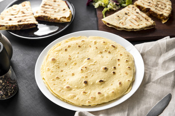 Mexican corn tortillas on a white plate on the dining table. In the background, hot quesadilla.