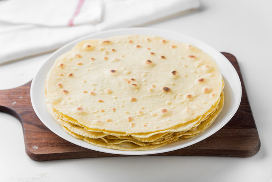 Mexican corn tortillas on a white plate on a wooden board. They can be used to make a burrito, takos and quesadilla.