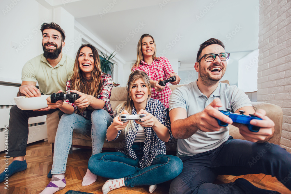 Wall mural group of friends play video games together at home, having fun.