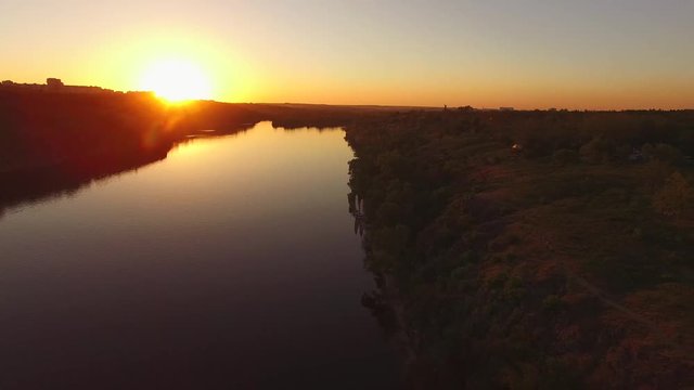 Flight over the rocky coast of a large river next to a city during sunset. Khortitsa Island, Dnieper River, Ukraine. Back light.