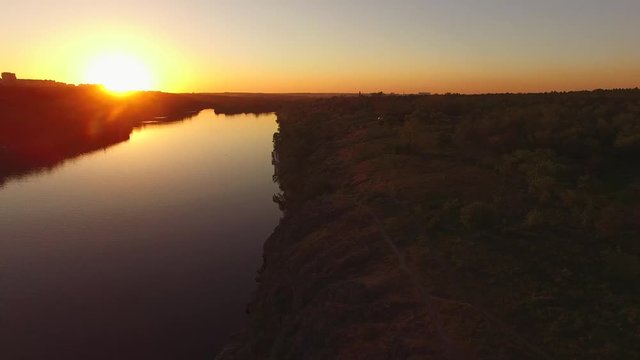 Aerial view of the rocky coast of a large river next to a city during sunset. Khortitsa Island, Dnieper River, Ukraine. Back light.
