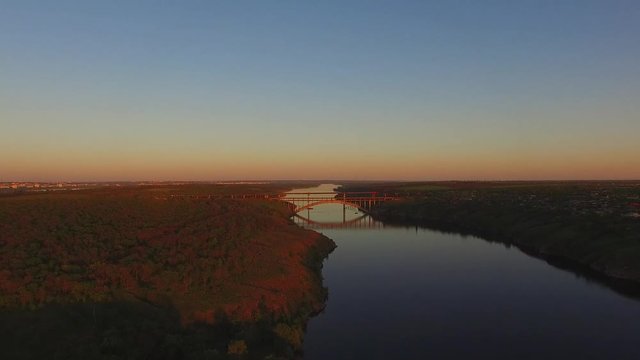 Flight along of the wooded coastline of a large river next to a large city during sunset. Dnieper River, Zaporozhye, Ukraine. Aerial view.
