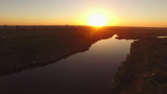 Flight over the wooded coast of a large river next to a city during sunset. Khortitsa Island, Dnieper River, Ukraine. Back light.