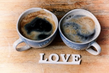Two blue cups of coffee and love inscription on a wooden table