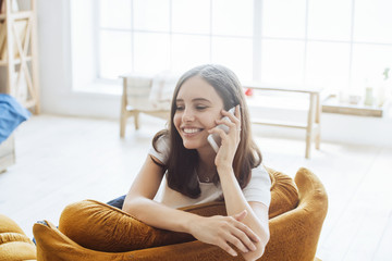 a beautiful woman is sitting comfortably in an orange sofa, smiling and talking on the phone