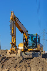 Obraz premium Yellow Excavator on the ground and electric lines on the blue sky