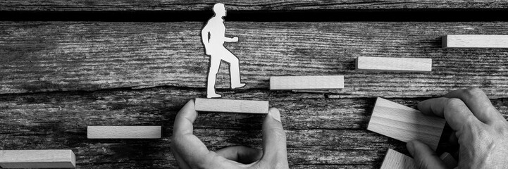 Man holding block as a small silhouette cutouts of a person walks up stairs
