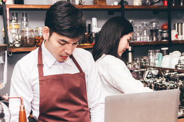 Portrait of couple barista working with coffee machine for making coffee and standing behind the counter bar in a cafe