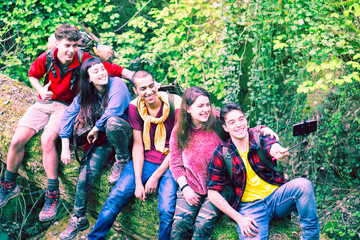 Multiracial group of young friends hikers taking selfie at national park on forest background - Row of teenagers having fun using mobile phone technology outdoors into the wild - Adventure concept