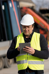 Engineer with safety vest and helmet looking at the construction site typing on a digital tablet computer