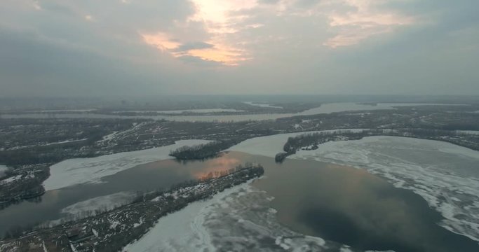 Frozen river in aerial view. Golden spike and sunny frosty day. Up over winter frozen river in sunset or sunrise time. Lateral and rear fly. Ice of frozen river during beautiful sunset.