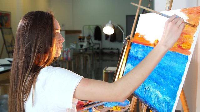 Woman artist following her inspiration painting her new picture at night in her workshop.