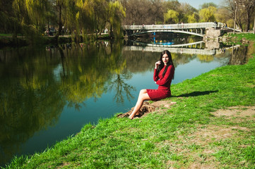 Fototapeta na wymiar beautiful young brunette with long hair in a park on a spring in spring among flowering trees in a red dress in hands holds magnolia flowers