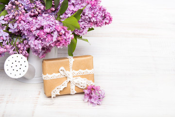 Lilac flowers and gift box on white wooden background, copy space