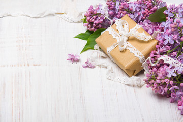 Obraz na płótnie Canvas Lilac flowers and gift box on white wooden background, copy space