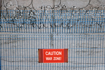 Iron fence with barbed wire. Metallic fence with red warning sign War zone!