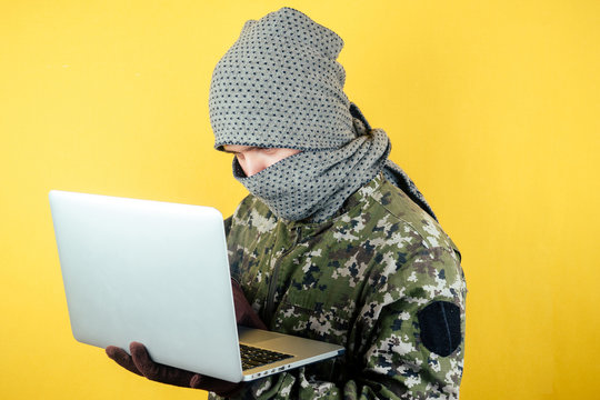 Portrait of a hacker man terroris in a camouflage and a mask is looking at the laptop. the concept of anonymity and terrorism hacking the system.