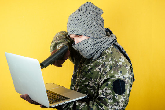 Portrait of a hacker man terroris in a camouflage and a mask is looking at the laptop. the concept of anonymity and terrorism hacking the system.