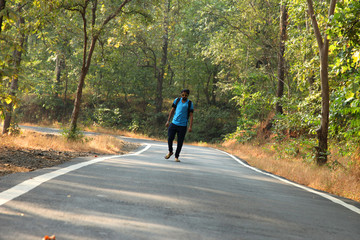 Travel concept man carrying backpack walking on the road passes through beautiful forests.
