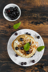 Sweet pancakes with black currant and powdered sugar on white plate on wooden rustic table, top view