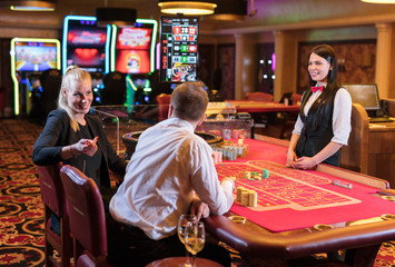 Cute lady casino dealer at Roulette table. Happy couple is playing Roulette.